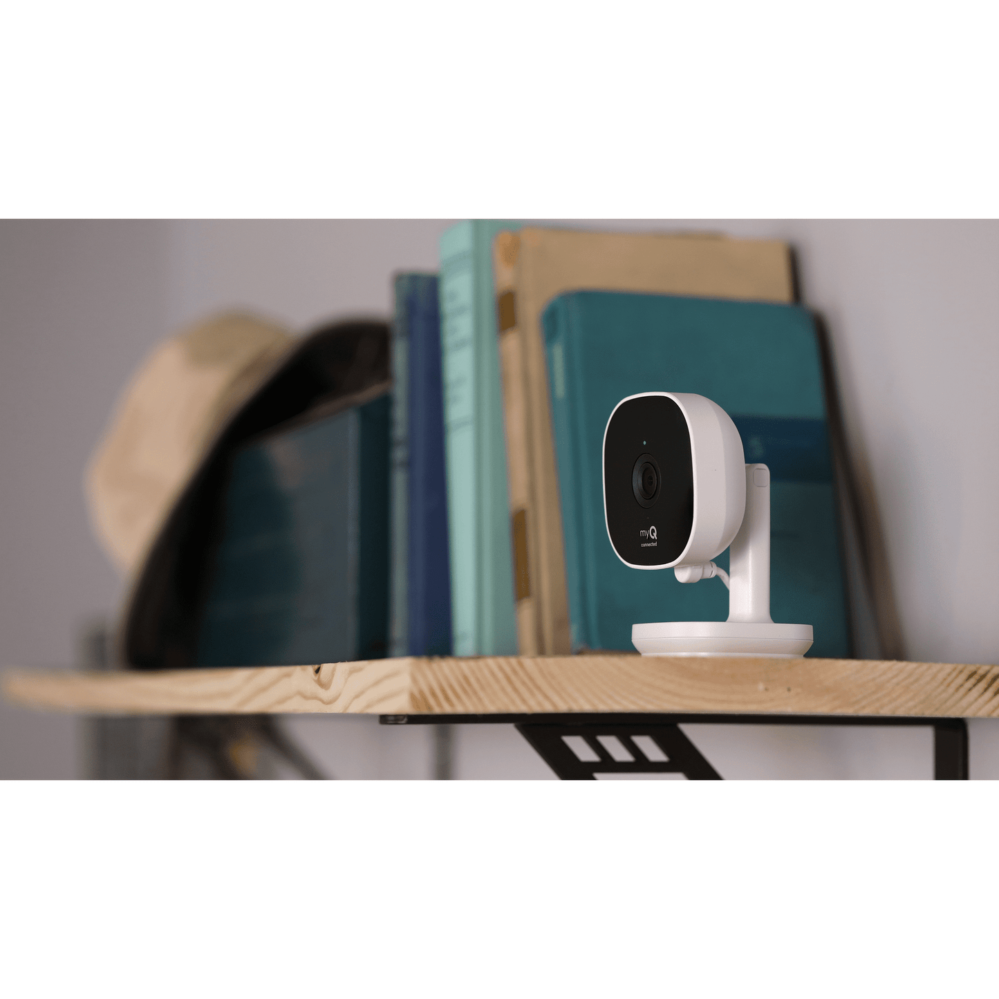 myQ smart indoor camera placed on wooden shelf near books in room setting