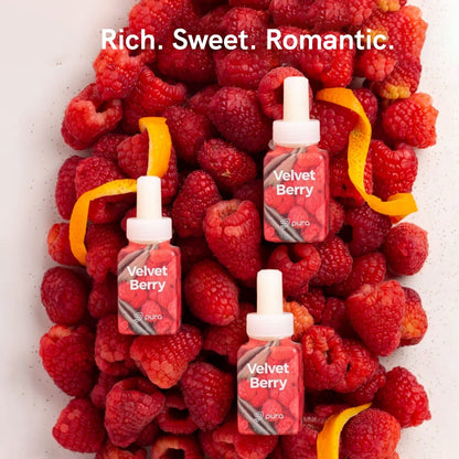 Three Velvet Berry fragrance refill bottles placed on fresh raspberries and orange peels with text 'Rich. Sweet. Romantic.'