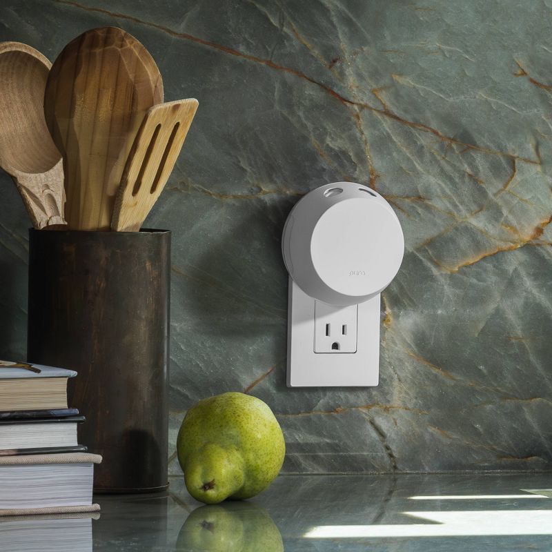 White Pura Smart Scent device plugged into a kitchen outlet near wooden utensils and a pear on stone countertop
