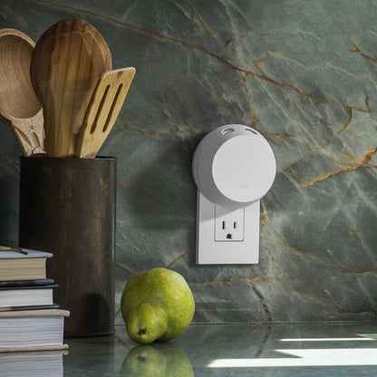 White Pura Smart Scent device plugged into a kitchen outlet near wooden utensils and a pear on stone countertop