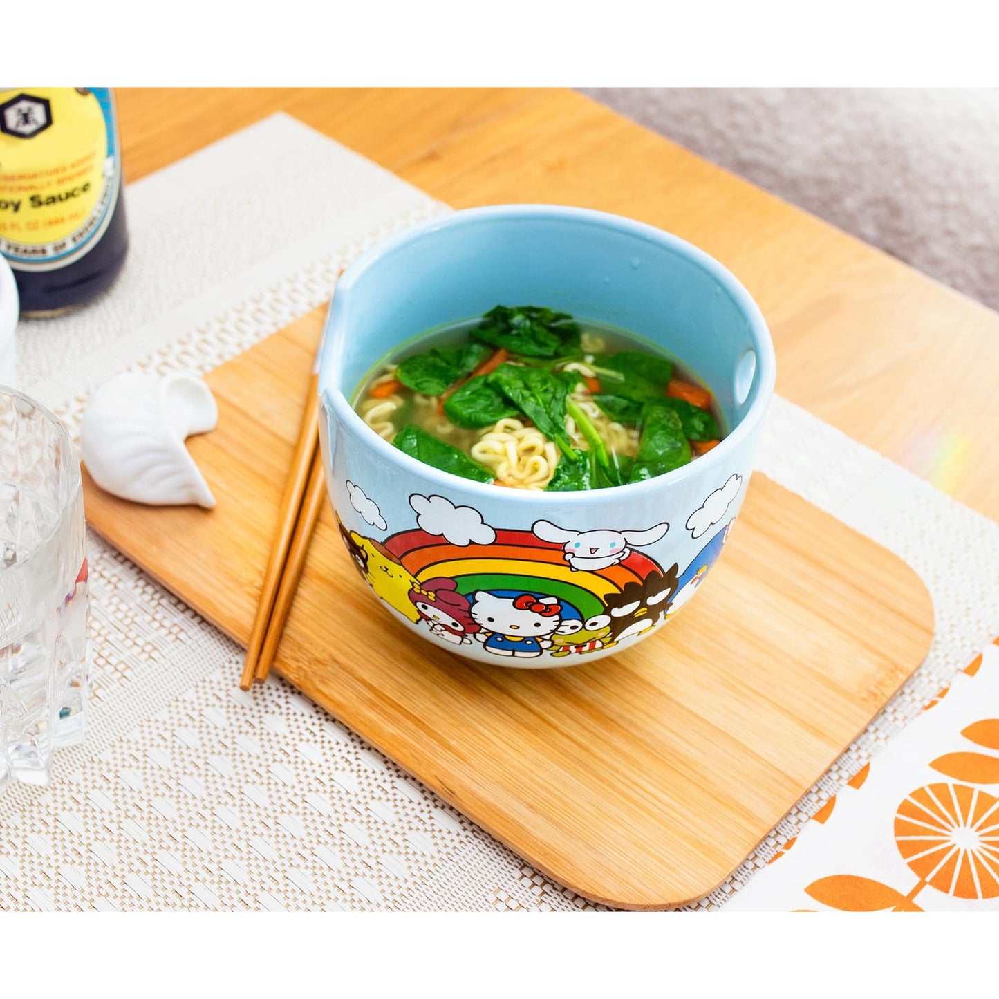 Light blue ceramic ramen bowl filled with soup and greens on a wooden board with chopsticks, in a bright dining area